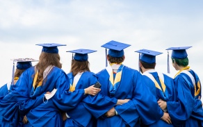 Six graduates in caps and gowns looking away from the camera with their arms around each other.
