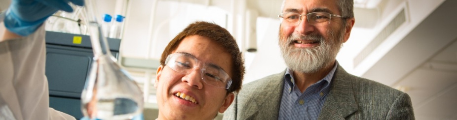 Dr Luis Colon works in a lab with a student wearing blue rubber gloves and holding a glass vial.