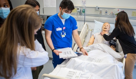 Group of people stand around a hospital bed.
