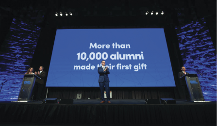UB executives are standing in front of a blue screen with the text: "More than 10,000 alumni made their first gift.".