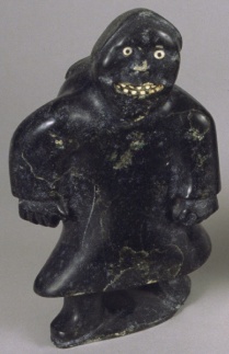 A soapstone sculpture of a figure covered in a garment with two hands and feet poking out. The figure has a toothy smile, white nose, and two wide eyes.