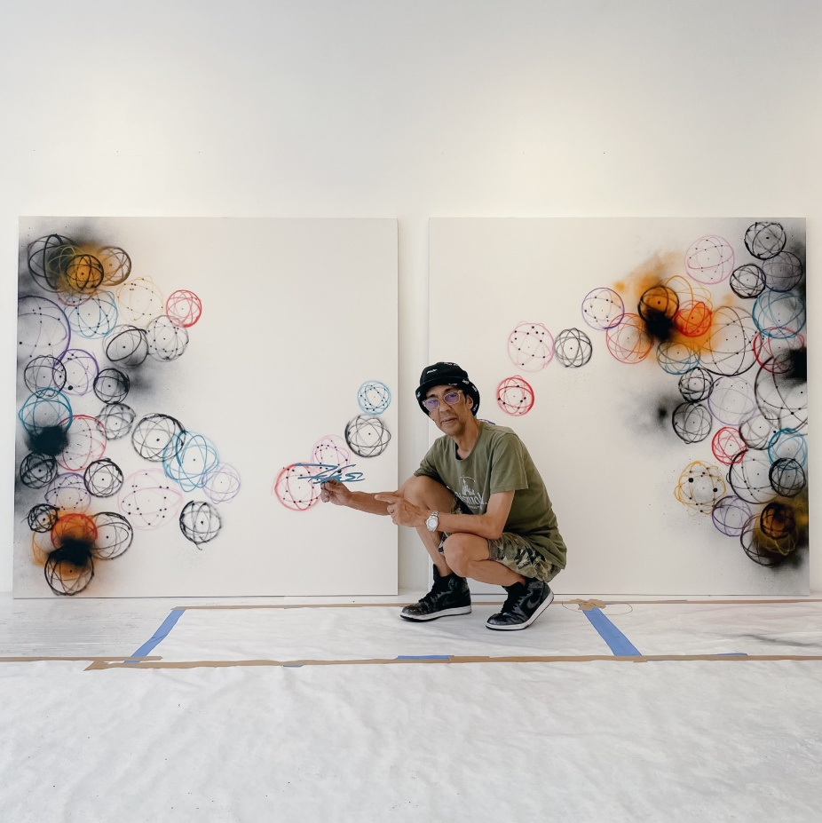 A photograph of artist Futura2000, kneeling in front of a canvas he's painting covered in atoms.