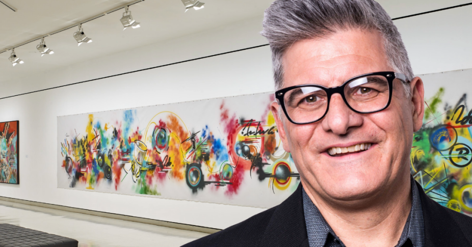 A headshot of Anthony Billoni, a white man wearing black rimmed glasses with gray short hair. He is pictured in front of an artwork by FUTURA 2000 in the UB Anderson Gallery.