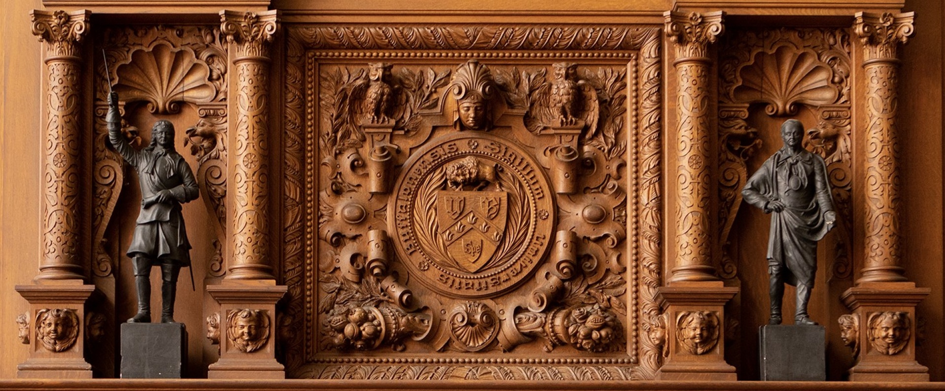 The UB seal is centered in an elaboraetly carved wooden mantel over the fireplace in the Health Sciences Library, Abbott Hall, South Campus.
