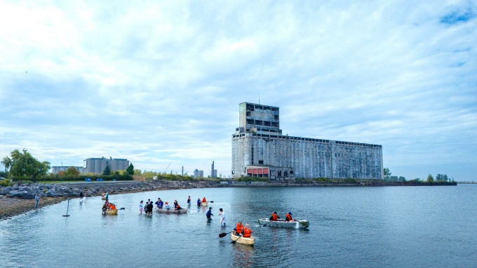 Architecture students in handmade canoes paddle near a grain elevator at Gallagher beach.