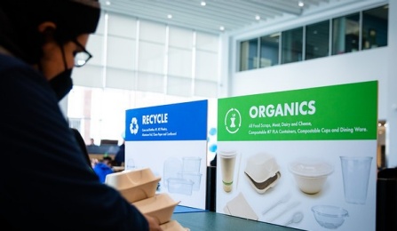 Student disposing of trash options at One World Café featured labeled bins “Recycle,” “Organics” and “Trash”.