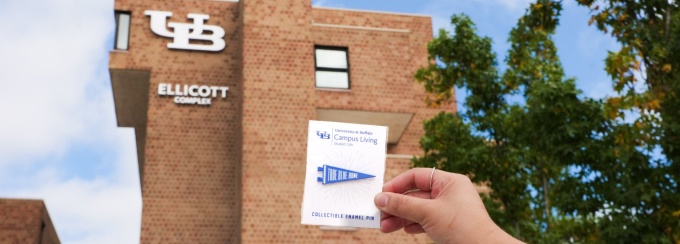 True Blue Home Pin held in front of the Ellicott Complex.