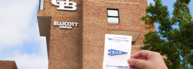 True Blue Home Pin held in front of the Ellicott Complex.