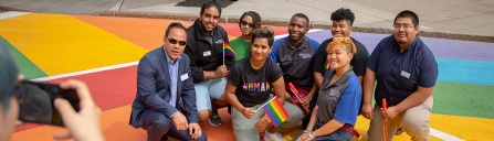 Students in a rainbow painted crosswalk holding rainbow flags.
