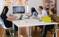 A diverse group of individuals sitting around a meeting table, looking at a shared computer screen. 