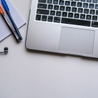 A laptop computer keyboard. On the left are earbuds, a notebook, and a blue and an orange pen. Photo Credit: Maya Maceka. 