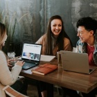 Three individuals sitting at a table with laptops open, laughing and learning. 