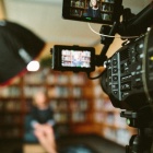 Image of a video camera filming an individual sitting in a chair. 