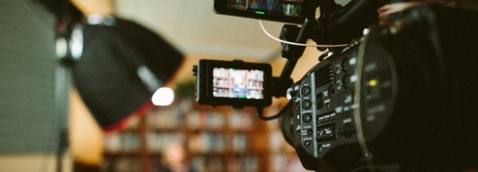 Image of a video camera filming an individual sitting in a chair. 