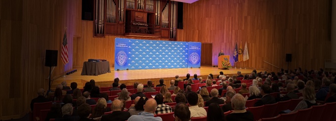 President Tripathi speaking at lectern on Slee Hall stage with UB and Celebration of Academic Excellence backdrop. 