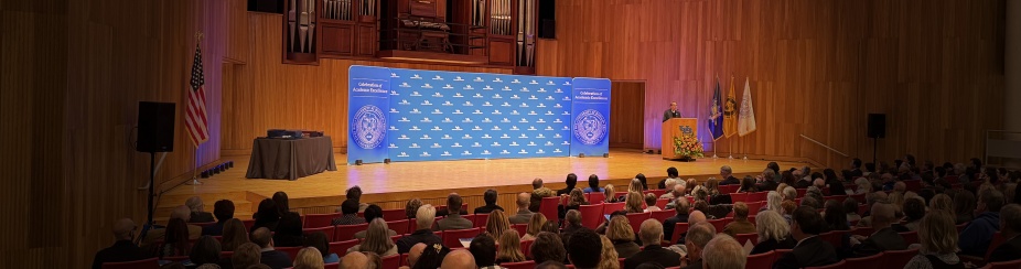 President Tripathi speaking at lectern on Slee Hall stage with UB and Celebration of Academic Excellence backdrop. 