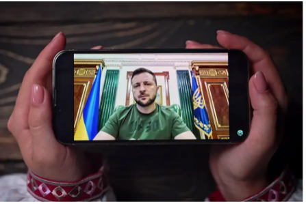 Photo of hands holding a phone showing a video of President Zelenskyy.