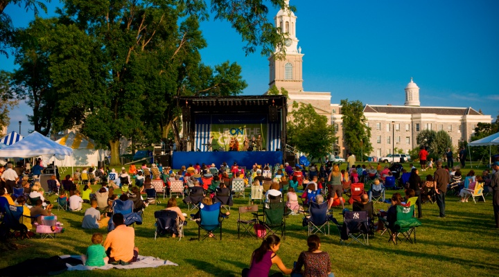 A crowd sits on the grass in front of a stage set up by Hayes Hall to listen to a concert that is a part of UB on the Green. 