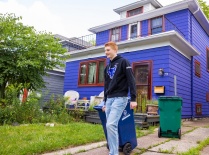 Student wheeling a trash bin to the curb outside a house.