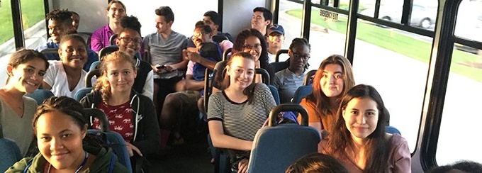 Students sitting on a bus and smiling.