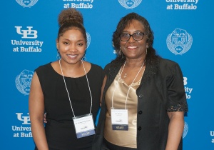 CSTEP Director with Administrative Assistant in front of UB logo backdrop.