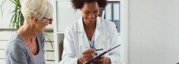 A doctor points to a clipboard as a patient watches.
