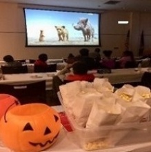A TV screen with a movie on it, and popcorn and jack-o-lanterns in the foreground.