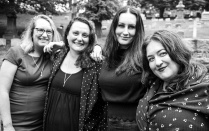 Black and white photo of four women outdoors, smiling at the camera. 