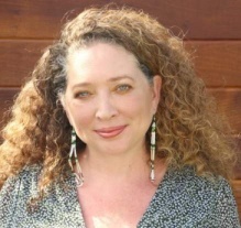 Mishuana Goeman, woman with long blonde curly hair wearing long beaded earing smiling. 