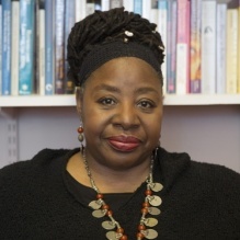 Loretta Ross, woman with updone hair in headwrap and red beaded earrings. Smiling. 