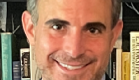 Man smiling at the camera in front of a bookshelf. 