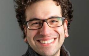 Man with curly hair and glasses, smiling at the camera. 