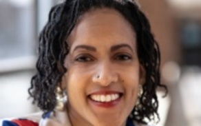 Woman with dark hair in a colorful blazer smiling at the camera.