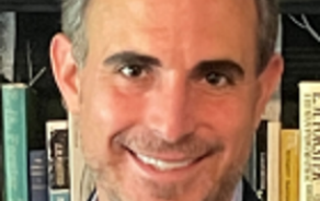 Man smiling at the camera in front of a bookshelf.