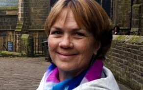 Woman outdoors wearing a white coat, smiling at the camera.