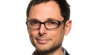 Man with short dark hair and glasses, smiling at the camera.