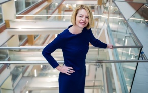 Woman in a blue dress, smiling at the camera.