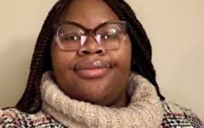 Photo shows a woman with glasses wearing a turtleneck sweater, smiling at the camera.