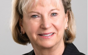 Photo shows a woman in a blazer, smiling at the camera.