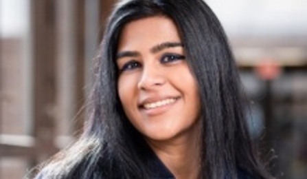 A woman with dark brown hair, wearing a blue shirt, smiling at the camera.