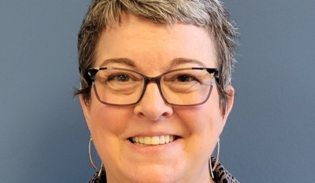 A woman with short hair, wearing glasses, smiling at the camera.