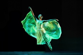 A graceful dancer from the Zodiaque company in mid-leap, lit with green light.
