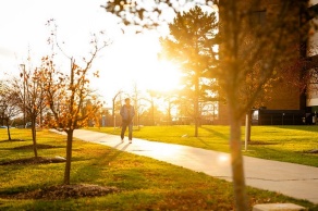 A person walks on a sidewalk near Hochstetter Hall in the late afternoon light, photographed in early December 2024.