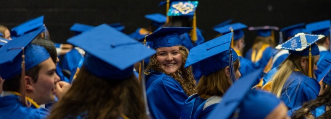 students sitting and laughing while wearing graduation caps and gowns. 