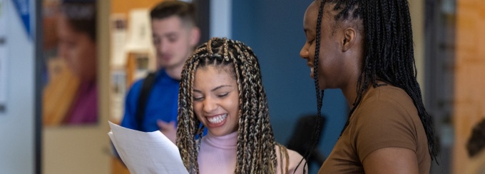 a student smiling while looking at a piece of paper with other students in a room. 