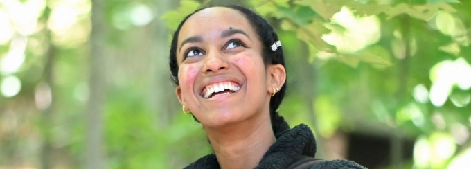 student smiling and looking up with trees and leaves in background. 