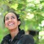 student smiling and looking up with trees and leaves in background. 