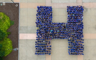overhead view of students in blue shirts forming a capital H.