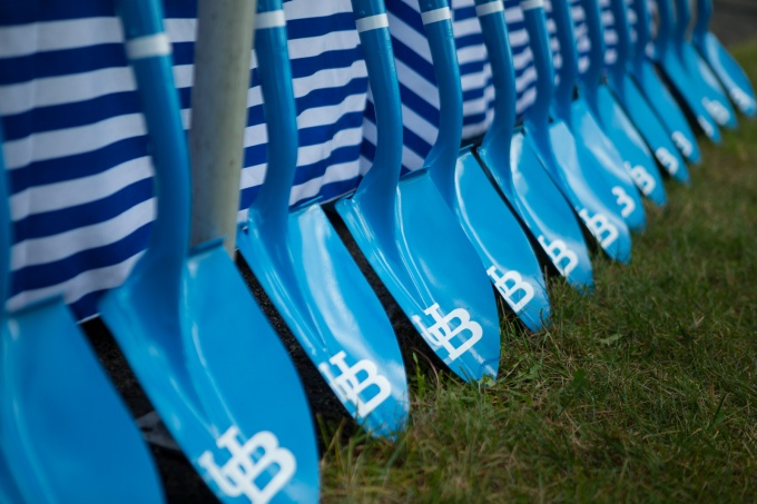 Shovels painted blue with UB logo lined up against a wall. 