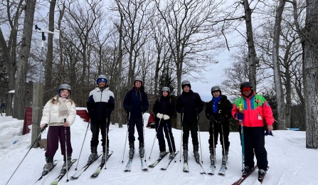 A group of students in ski gear standing in a group with their ski instructor.